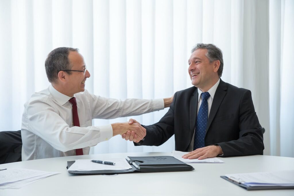 Two men in an office setting smile while shaking hands