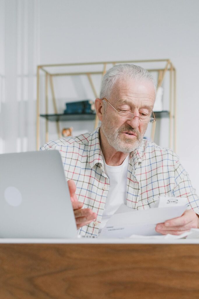 Older man with glasses, sitting at a desk and looking over a pile of paperwork.