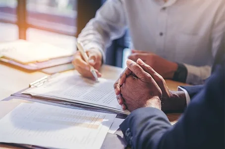 Two people at a table, one signing a document on a clipboard while the other listens