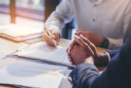 Two people at a table, one signing a document on a clipboard while the other listens