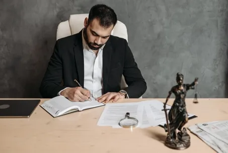Male lawyer writing in a notebook with Lady Justice statue on desk