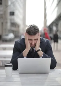 Stressed man holding face at laptop