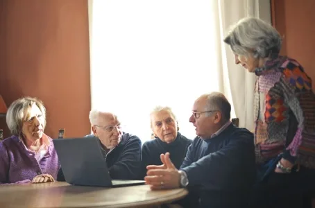 Group of five senior adults gathered around a laptop screen