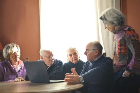 Group of five senior adults gathered around a laptop screen
