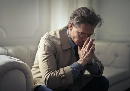 Stressed man with clasped hands on sofa