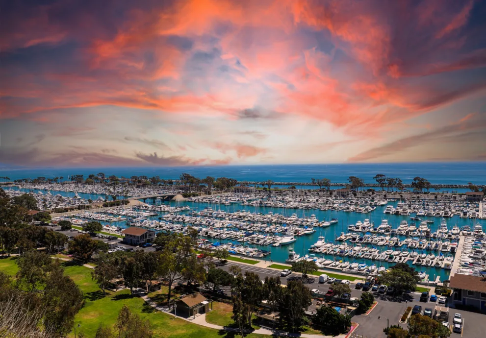 An aerial view of Dana Point Harbor filled with numerous boats under a vibrant sunset sky.