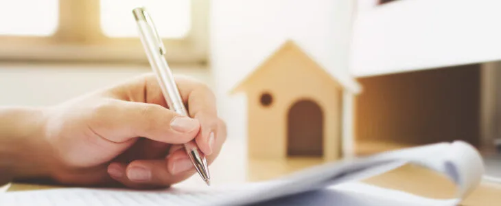 Close up hand of man signing signature loan document to home ownership. Mortgage and real estate property investment